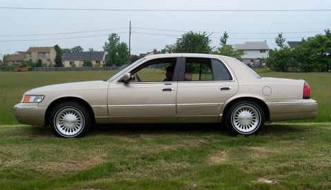 1999 Mercury Marquis - Side profile of a 1999 Mercury Marquis sedan parked outdoors on a grassy area.