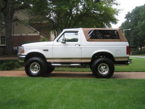 1996 Ford Bronco - Driver-side profile of a lifted white 1992-96 Ford Bronco with tan Eddie Bauer-style lower two-tone, fitted with a tan soft top in place of…