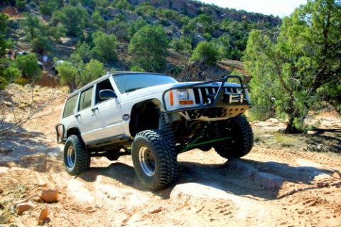 1997 Jeep TJ - This modified Jeep Cherokee XJ is navigating a rocky off-road trail under a clear sky.