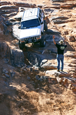 1997 Jeep TJ - A white Jeep Cherokee tackles a challenging rocky trail, guided by a person. The registry's claim of it being a 1997 Jeep TJ appears inaccu…