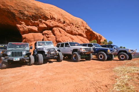 1997 Jeep TJ - A convoy of off-road vehicles is parked in a desert landscape with a prominent red rock overhang.
