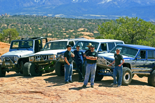 Four modified Jeeps parked on a dirt trail with mountains in the background