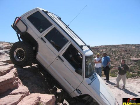 1997 Jeep TJ - A white Jeep Cherokee XJ navigates a steep rock obstacle with onlookers observing the challenging off-road maneuver.