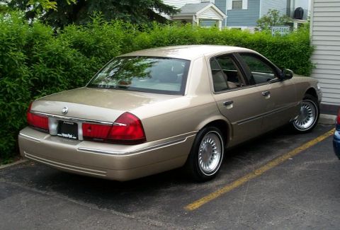 1999 Mercury Marquis - A tan sedan is parked in a lot with a yellow line on the asphalt.
