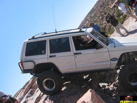 1997 Jeep TJ - A white 1997 Jeep Cherokee XJ navigates a rocky off-road trail under a clear blue sky.