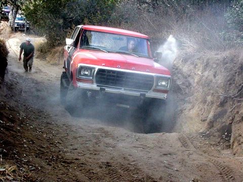 1979 Ford Bronco - A red 1979 Ford Bronco navigates a dusty off-road path, with another vehicle ahead.