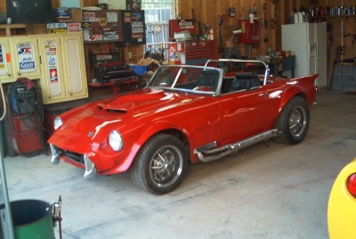 1972 Ford Ranchero - A red convertible sports car with a hood scoop and side pipes is parked inside a cluttered garage.