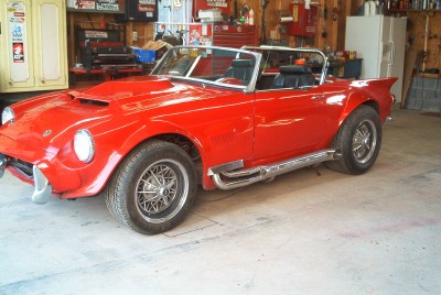 1972 Ford Ranchero - A red convertible sports car with chrome side pipes and a prominent hood scoop is parked inside a cluttered garage.