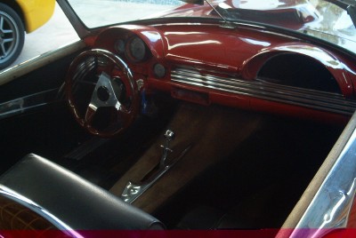 1972 Ford Ranchero - Interior view of a red car, a wooden steering wheel and dashboard. A yellow car is partially visible in the background.