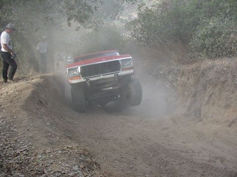 1979 Ford Bronco - A red SUV navigates a dusty, off-road trail with a person watching from the side.