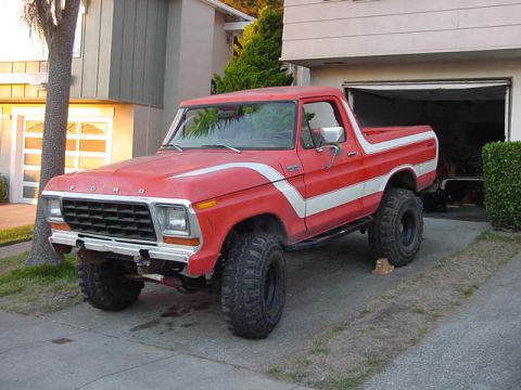 1979 Ford Bronco - This red Ford Bronco is parked in front of a garage with a white stripe down its side.