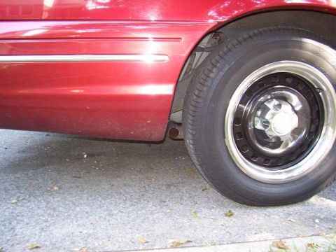 1999 Ford Crown Victoria - Close-up of a red car's lower body panel and wheel.