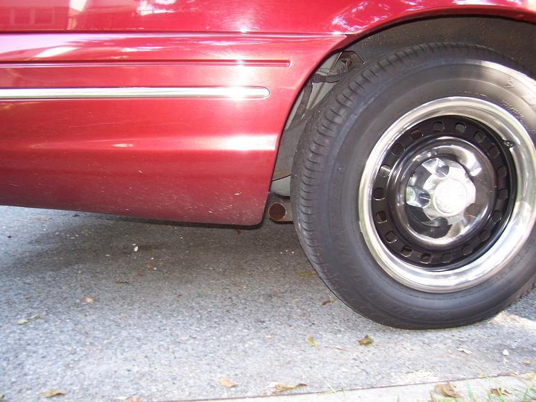 Red car side view, showing lower body panel with chrome trim and a black steel wheel with a chrome lip