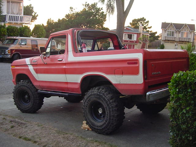 Lifted red-and-white Ford Bronco on large mud tires parked at a curb