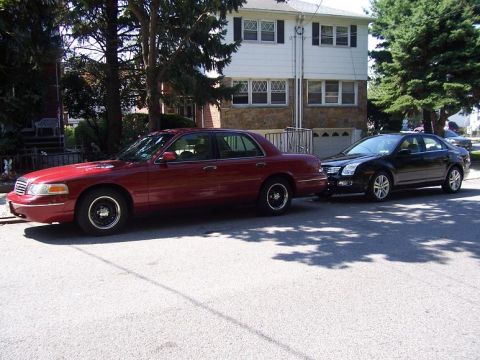 1999 Ford Crown Victoria - A red 1999 Ford Crown Victoria is parked on a residential street next to a black sedan.