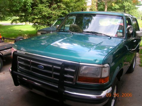 1996 Ford Bronco - A green Ford Bronco with a brush guard is parked in a driveway next to another vehicle.