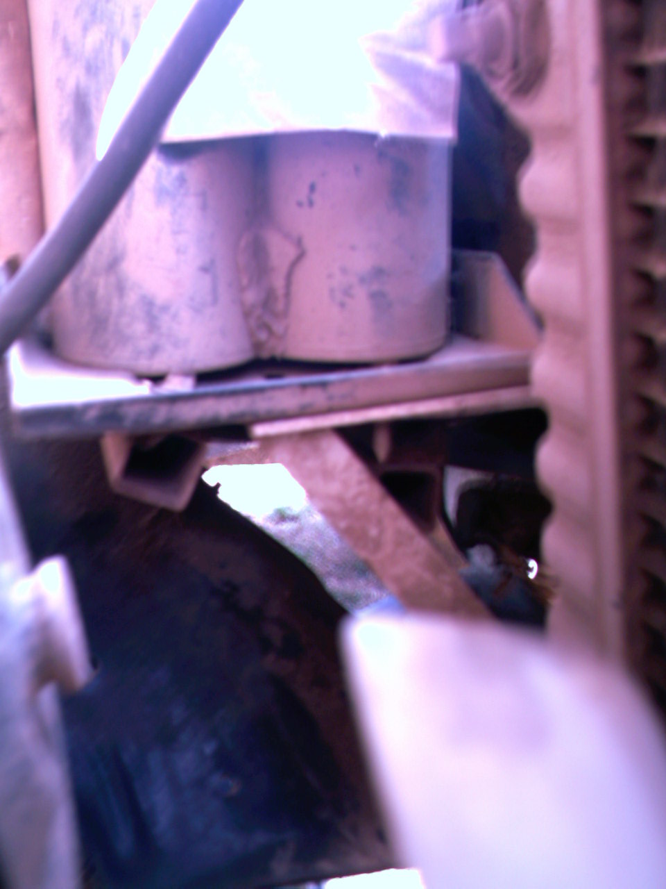 Engine bay with two cylindrical components, metal brackets, and part of a radiator