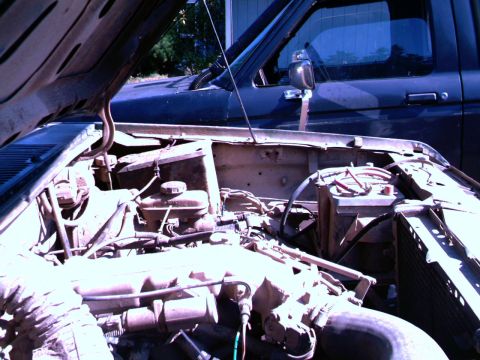 1987 Ford Bronco II - The engine bay of a 1987 Ford Bronco II, dual batteries and a glimpse of another vehicle behind it.