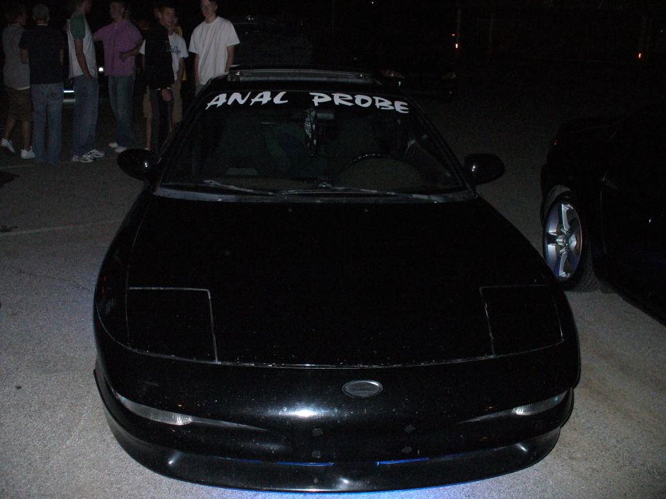 Black car with pop-up headlights and "ANAL PROBE" banner