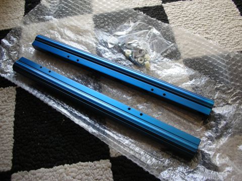 1998 Ford Crown Victoria - Two blue anodized aluminum extruded rails with mounting holes lie on bubble wrap beside a bag of hardware on a checkered rug.