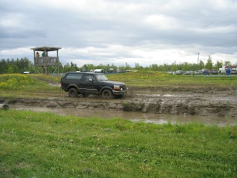 1978 Ford Bronco - SUV driving through a muddy obstacle course under a cloudy sky.