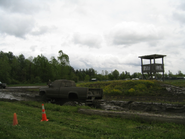 Muddy pickup truck stuck in a mud pit with a wooden observation tower in the background