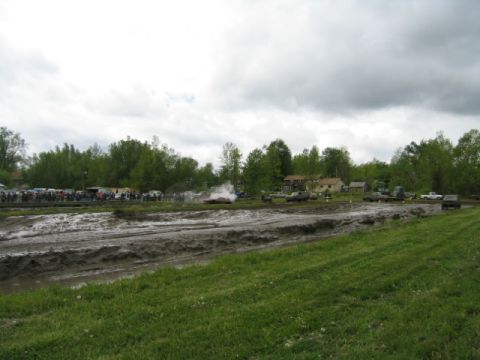 1978 Ford Bronco - A muddy field with various vehicles and spectators gathered under an overcast sky.