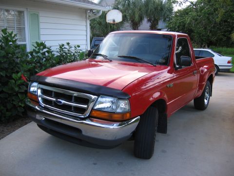 1974 Ford F-100 - Red Ford Ranger pickup truck parked in a driveway with a house and trees. A white car is visible in the background.