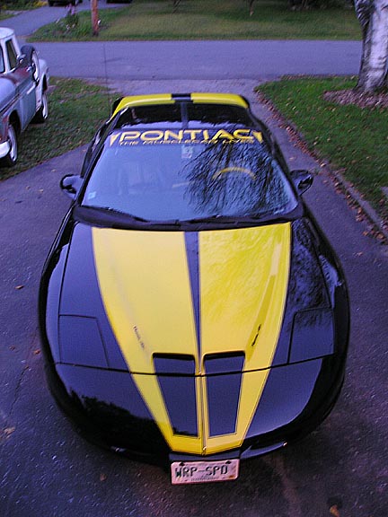 1984 Pontiac Fiero - A black and yellow Pontiac Firebird is parked in a driveway, with another vehicle visible to the left.