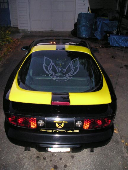 1984 Pontiac Fiero - Rear view of a black 1994 Pontiac Trans Am with yellow racing stripes and a bird decal.