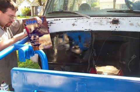 1979 Ford Bronco - A man holds a magazine while looking into the open engine bay of a vehicle.
