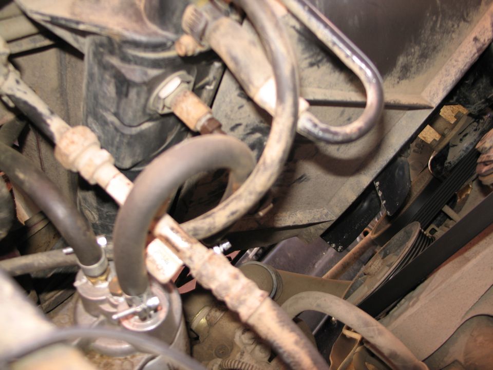 Close-up of dusty A/C lines, hoses and accumulator in an engine bay next to the serpentine belt
