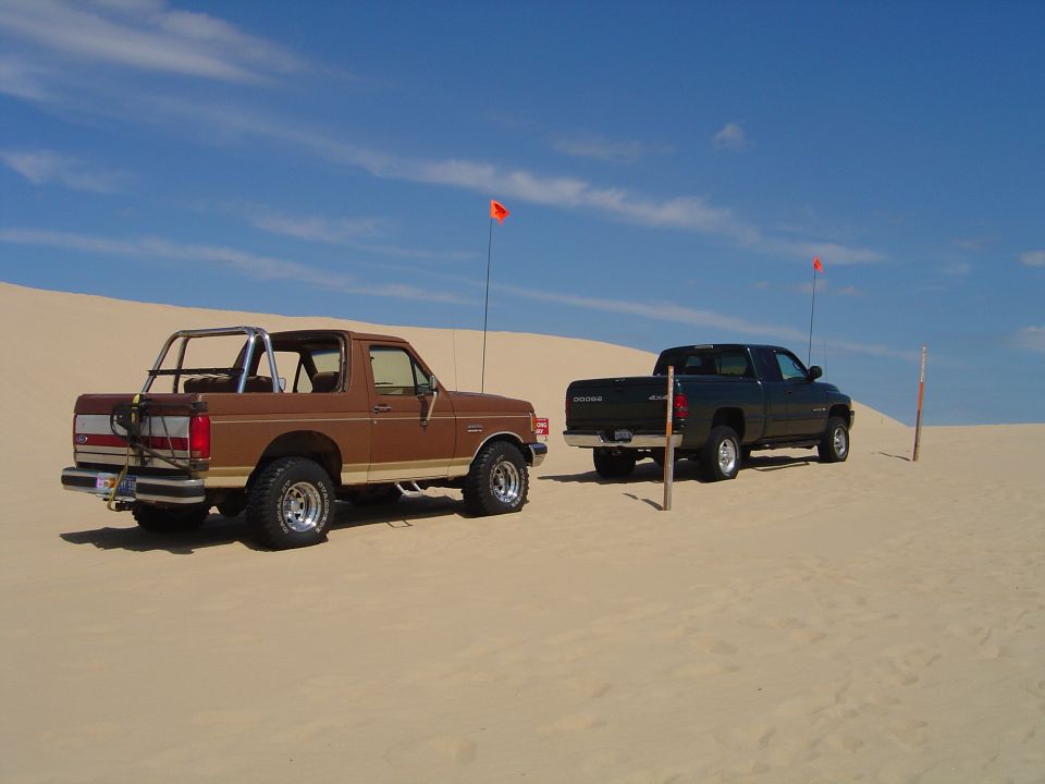 Brown 1991 Ford Bronco and dark green Dodge Ram on sand dunes