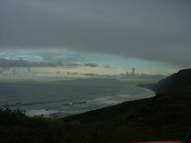 Overcast sky over ocean and coastline with waves crashing
