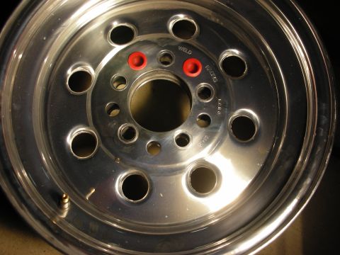 1998 Ford Crown Victoria - Close-up of a polished aluminum Weld racing wheel face showing the lug pattern, lightening holes, red accents, and stamped markings.