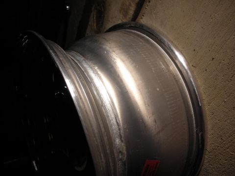 1998 Ford Crown Victoria - Side view of a polished aluminum wheel barrel with a black outer lip and a red warning label, photographed on a concrete floor.