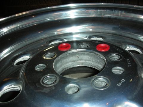 1998 Ford Crown Victoria - Close-up of a polished aluminum Weld wheel center with red lug-hole accents and stamped markings around the hub bore.