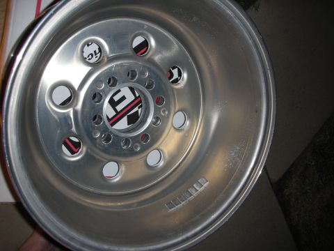 1998 Ford Crown Victoria - silver steel racing wheel with a vented multi-hole center and small black-and-red decals rests on a cardboard surface.