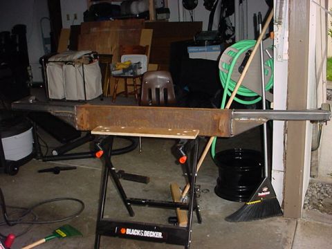 1979 Ford Bronco - A cluttered garage scene features a workbench with tools, a broom, and a coiled green hose.