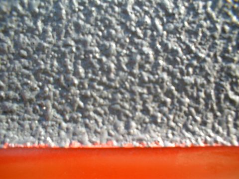 1995 Ford F-150 - Extreme close-up of a spray-on bedliner edge, showing the heavily textured gray rubberized coating meeting a strip of glossy red painted bo…