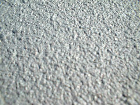 1995 Ford F-150 - Extreme close-up of a rough, gritty gray concrete or asphalt surface filling the entire frame; no vehicle or vehicle part is visible.