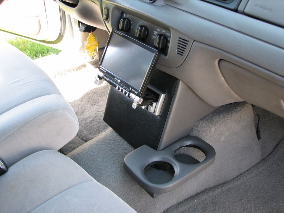 Car interior showing a custom console with a screen and stereo, plus a double cup holder
