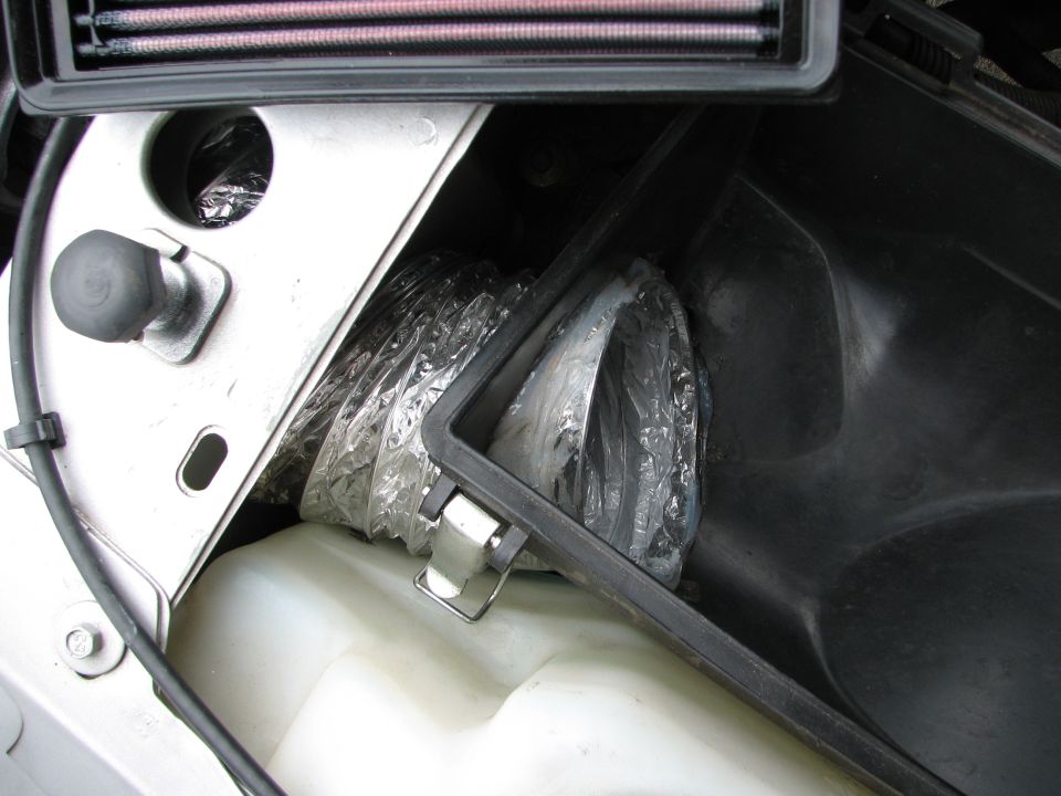 Engine bay showing a flexible duct inside the airbox, next to a white fluid reservoir