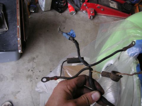 1999 Jeep Grand Cherokee - A hand holds a black wiring harness with metal ring terminals and blue tape against a garage floor background.