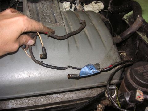 1999 Jeep Grand Cherokee - A hand manipulates a section of the engine's wiring harness, showing electrical connections and a blue tape marker.