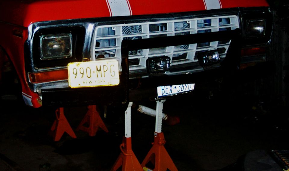 Red truck front end on jack stands, showing grille, headlights, and New York plates