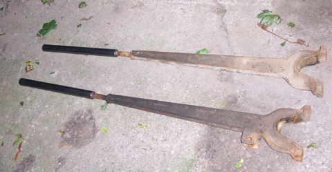1978 Ford Bronco - These are two old suspension control arms, likely from a vehicle, resting on a concrete surface.