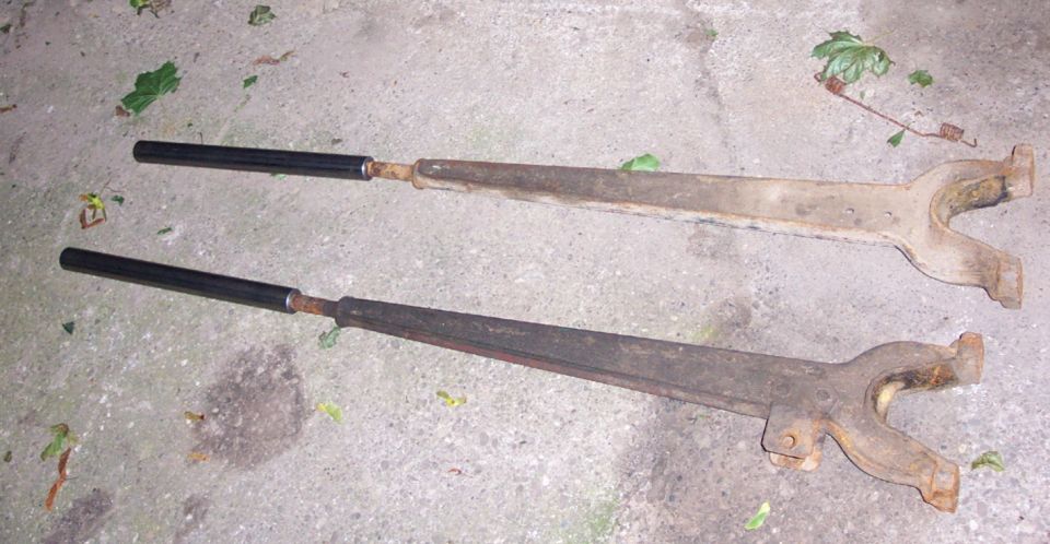 two rusty control arms with black ends lying on concrete
