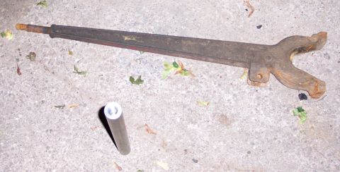 1978 Ford Bronco - A rusty metal automotive part lies on concrete next to a cylindrical piece, with some leaves scattered around.