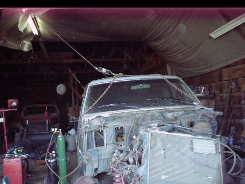 1984 Ford Bronco - The front end of a 1984 Ford Bronco is hoisted by chains in a garage, revealing its disassembled state and exposed radiator.